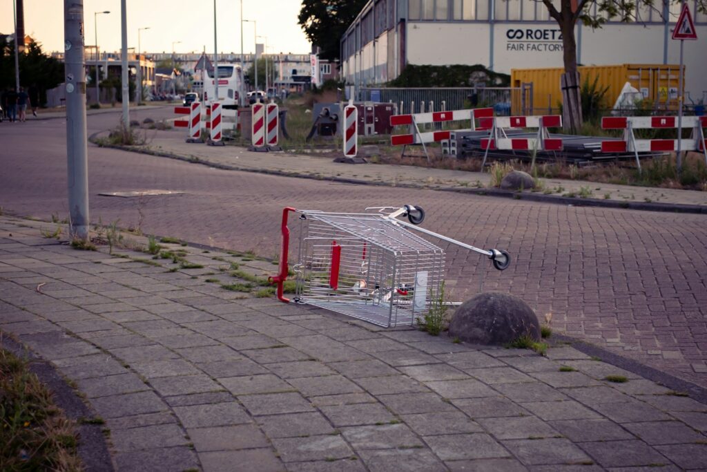 Shopping cart overturned on sidewalk next to road.